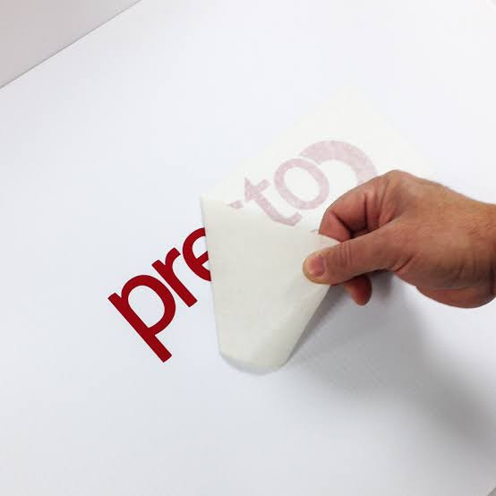Hand peeling sticker from red text surface.