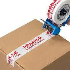 Person's hand holding a tape dispenser and sealing a fragile label onto a cardboard box