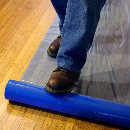 Person standing on top of a blue plastic sheet on a wooden floor