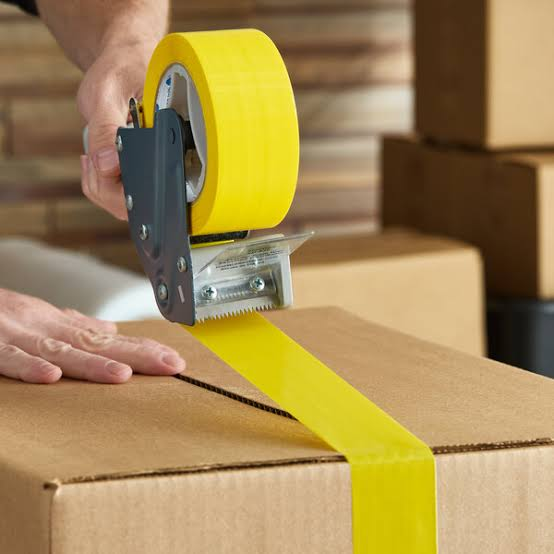 Sealing a cardboard box with yellow tape.